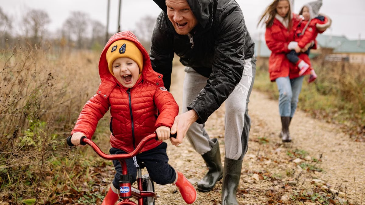 Father helping son ride a bicycle on a fall day while mother and daughter watch.